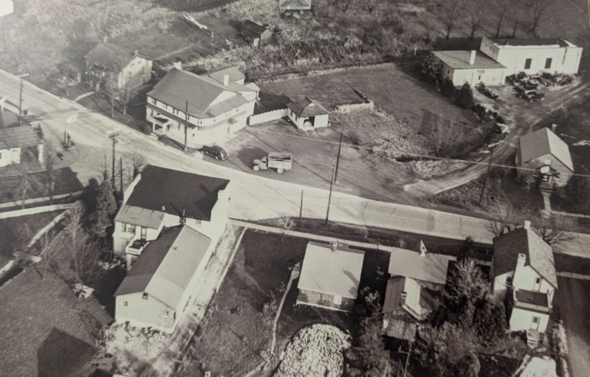 A historic black‑and‑white aerial photograph of the Lancaster Smokehouse property showing the early parking lot, surrounding homes, and mid‑century roads; this same print is also displayed at the Bridgeport Community Centre as part of its local history collection.